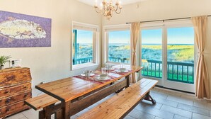 A dining area with a wooden table, benches, and a view of the beach through large windows.