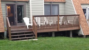 Une maison dotée d’une terrasse en bois, d’une porte-fenêtre coulissante et d’un petit porche avec des chaises.