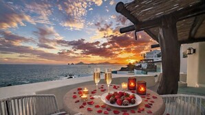 A table set with a plate of strawberries, two glasses of champagne, and candles, overlooking a sunset over the sea.