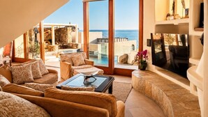 A spacious living area with a large window overlooking a pool and the sea.
