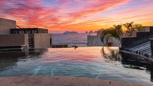 A pool with a sunset view, a ship in the distance, and a palm tree.