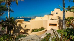 A coastal building with a view of the sea, palm trees, and a clear sky.