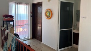 Habitación de hotel con puerta corredera de vidrio, puerta de madera, calentador pequeño fijado a la pared y perchero con toallas dobladas.