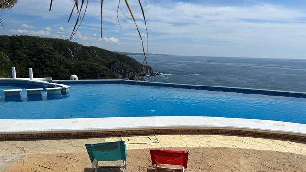 Una piscina con vista al océano, dos sillas de playa y un patio de piedra.