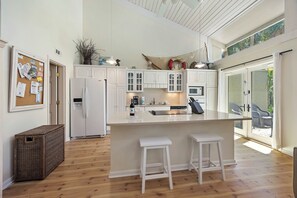 A modern kitchen with white cabinetry, a central island with stools, and a view to the outside.