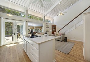 A spacious open-plan living area with a large island, wooden flooring, and a staircase with a railing.