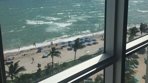 A beach view from a window, including the ocean, beach umbrellas, and palm trees. - RIGHT ON THE BEACH-Direct Oceanview Luxury 2 Bed/2Bath Condo in the Tides Resort (Hollywood)