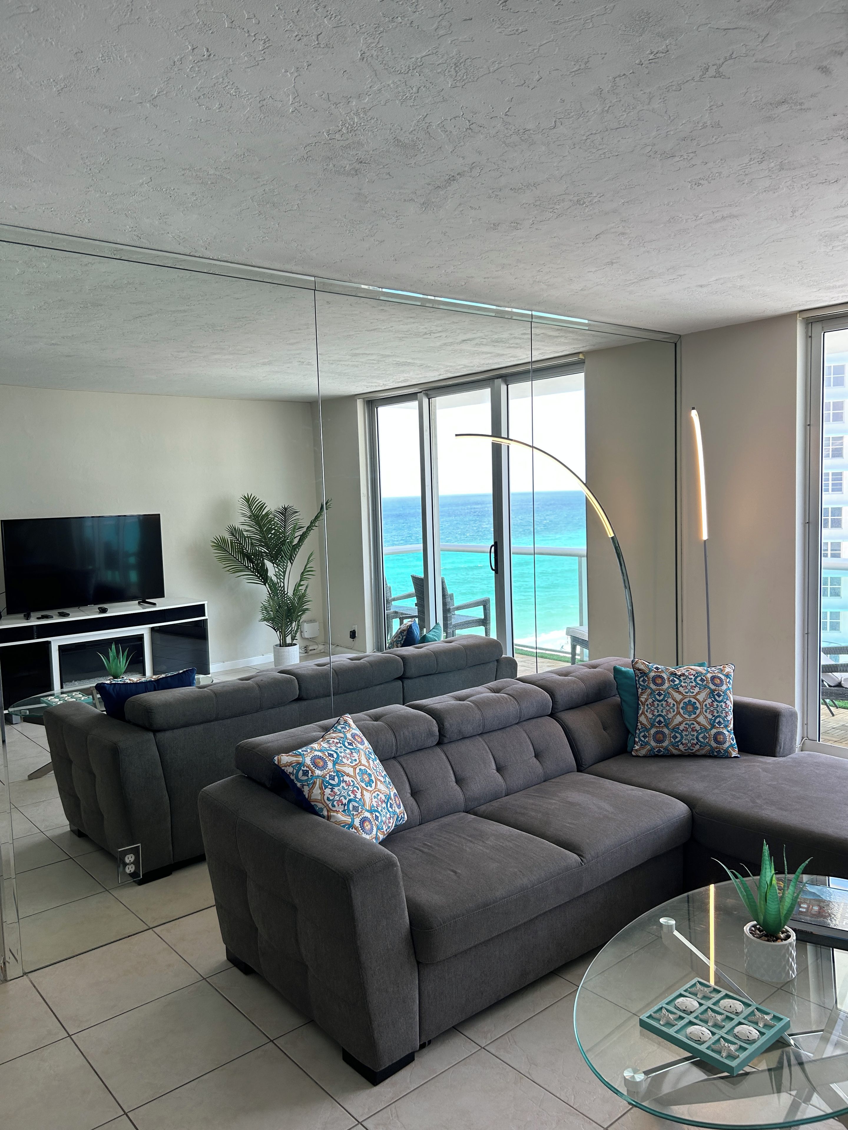 A modern living room with a sectional sofa, a flat-screen TV, and a glass coffee table.