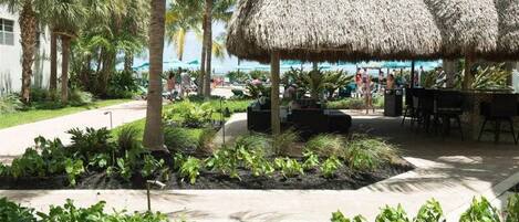 A thatched-roof outdoor seating area with palm trees and a view of the ocean.