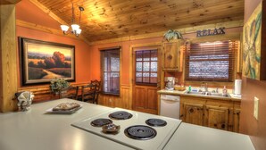 A kitchen with wooden cabinets, a white stove, and a painting on the wall. - Family Tyme #78 - Charming & Clean Log Cabin! (Sevierville)