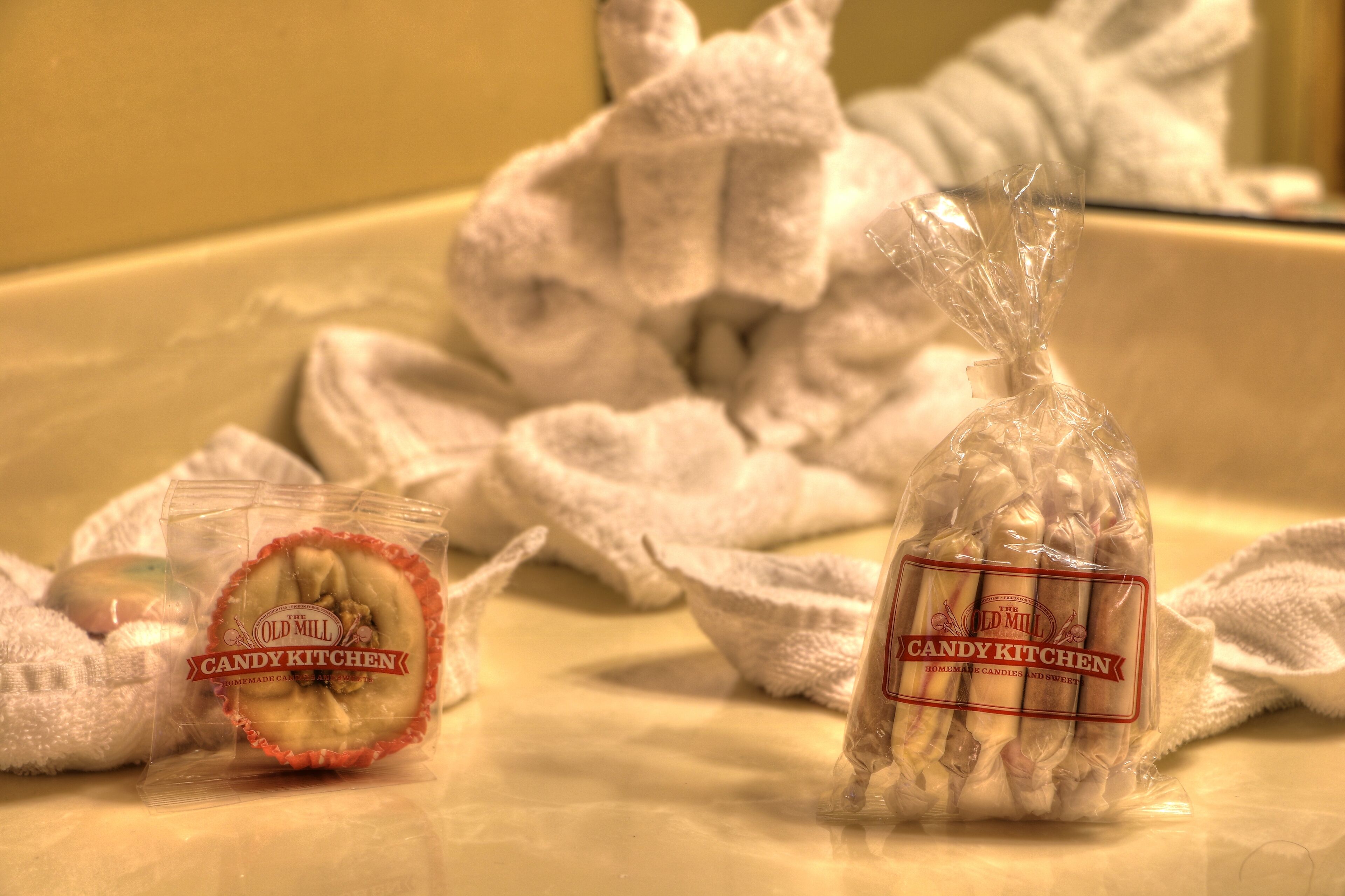 A bathroom with a sink, a towel, and two plastic containers labeled 'The Old Mill Candy Kitchen' with homemade candies and sweets.