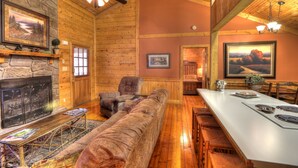 A cozy log cabin interior with a stone fireplace, wooden furniture, and a dining area. - Family Tyme #78 - Charming & Clean Log Cabin! (Sevierville)