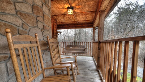 A wooden porch with stone walls, wooden benches, and a railing overlooking a forested area. - Family Tyme #78 - Charming & Clean Log Cabin! (Sevierville)