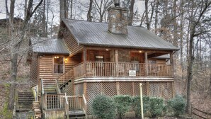 A log cabin with a stone chimney, wooden balcony, and a staircase leading to the entrance. - Family Tyme #78 - Charming & Clean Log Cabin! (Sevierville)