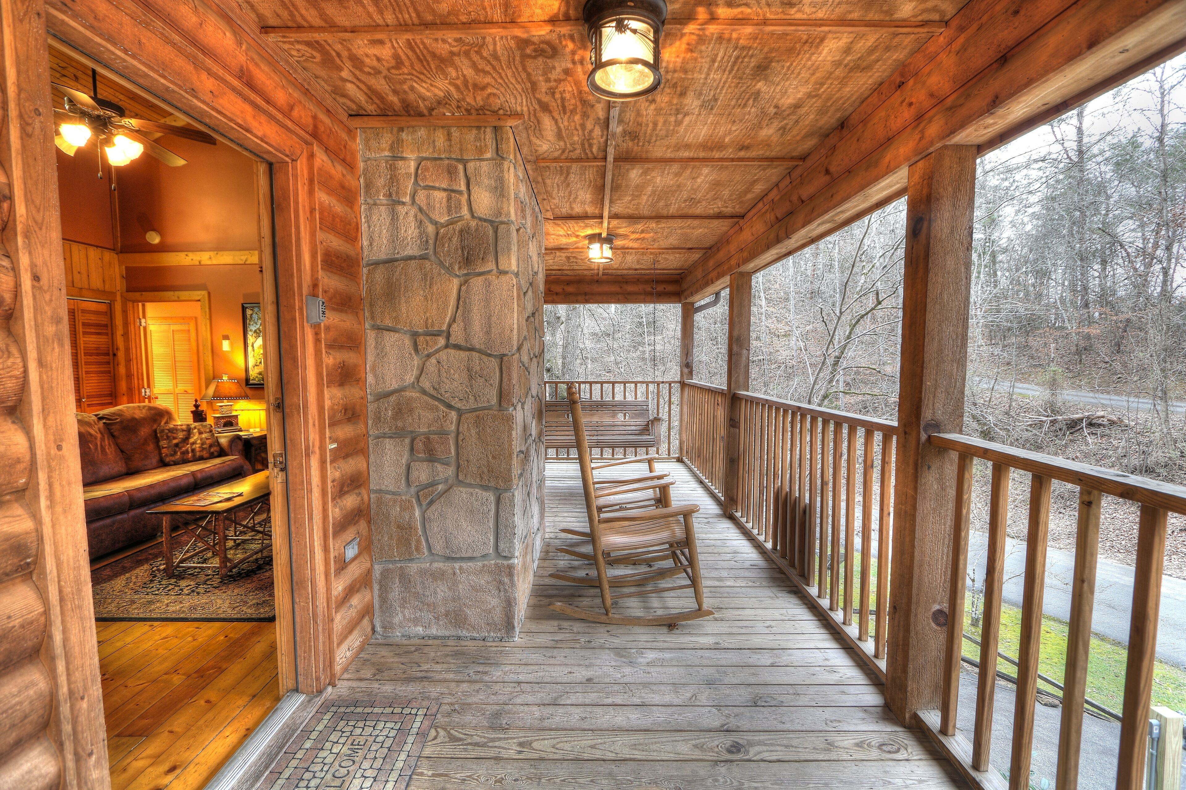A wooden porch with a stone pillar, rocking chairs, and a view of the surrounding forest.