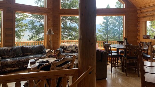 A cabin interior with a wooden dining area, a sofa, and a large window overlooking trees.