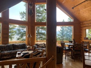 A cabin interior with a wooden dining area, a sofa, and a large window overlooking trees.