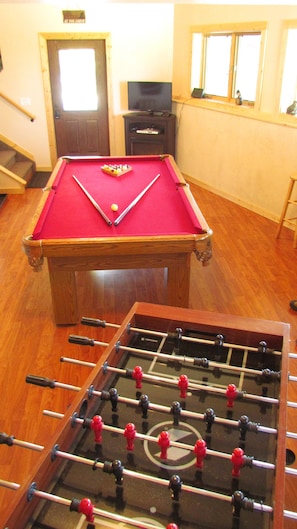 A pool table with a red felt surface and a foosball table with red and black figures.