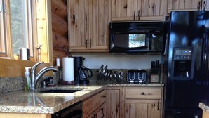 A kitchen with wooden cabinets, a stainless steel sink, a microwave, and a refrigerator.