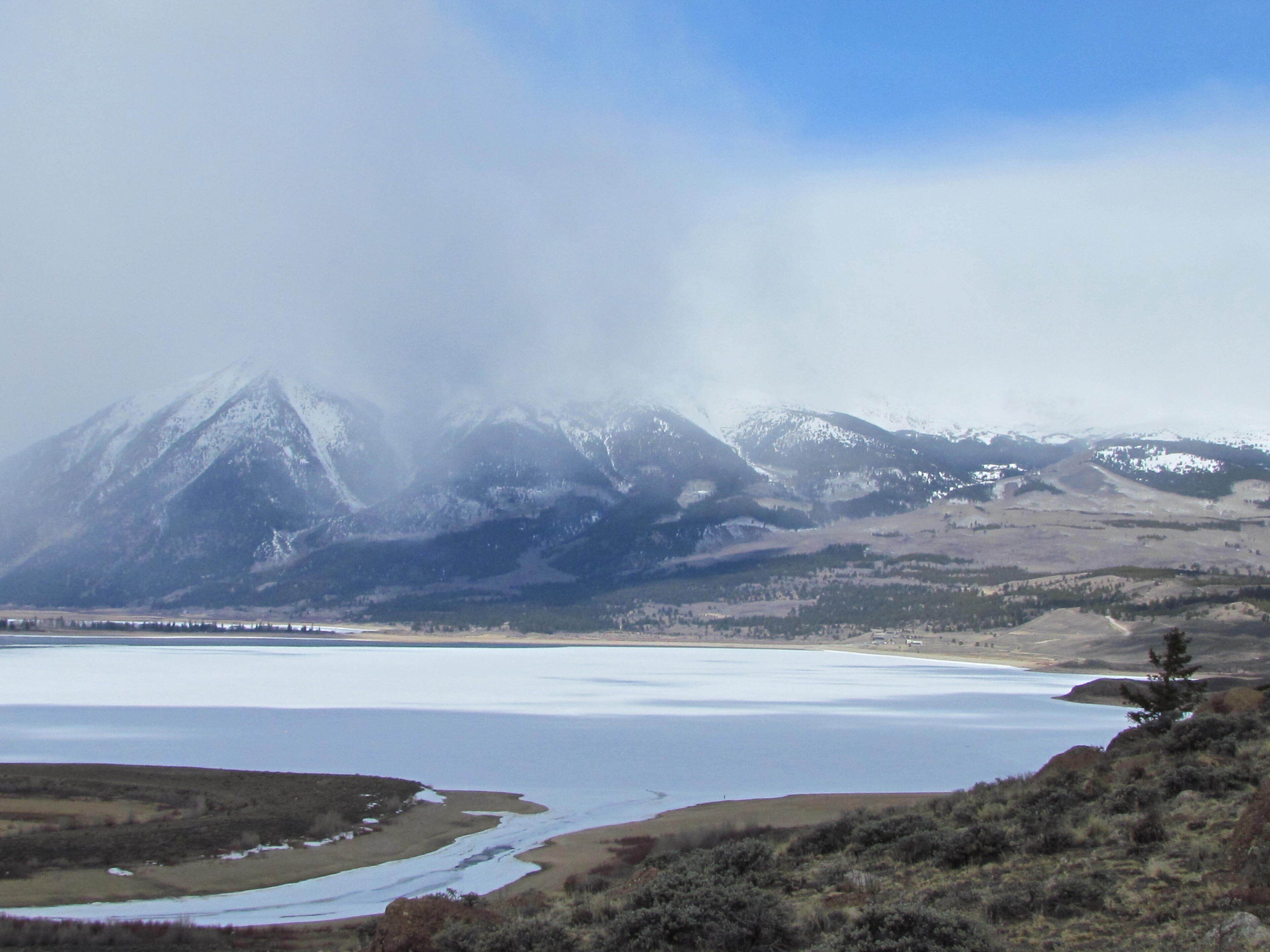 Un paysage montagneux avec un lac et des sommets enneigés en arrière-plan.