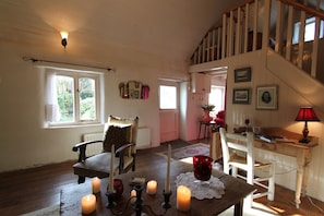 A cozy room with a wooden table, candles, and a staircase. - Charming cottage with a hot tub and deck overlooking a stream. Amazing kitchen! (Castleisland)