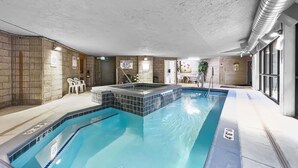 En indendørs swimmingpool med flisekant, en livredderstation og et siddeområde med stole.