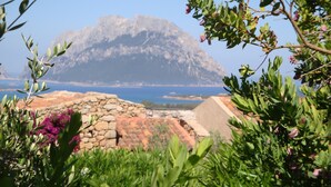 A mountainous landscape with a stone structure in the foreground and a view of the sea in the background. - Holiday apartments L'Ea di Lavru 
SEA VIEW 3-rooms apartment-TOP INTERIOR DESIGN (Porto San Paolo)