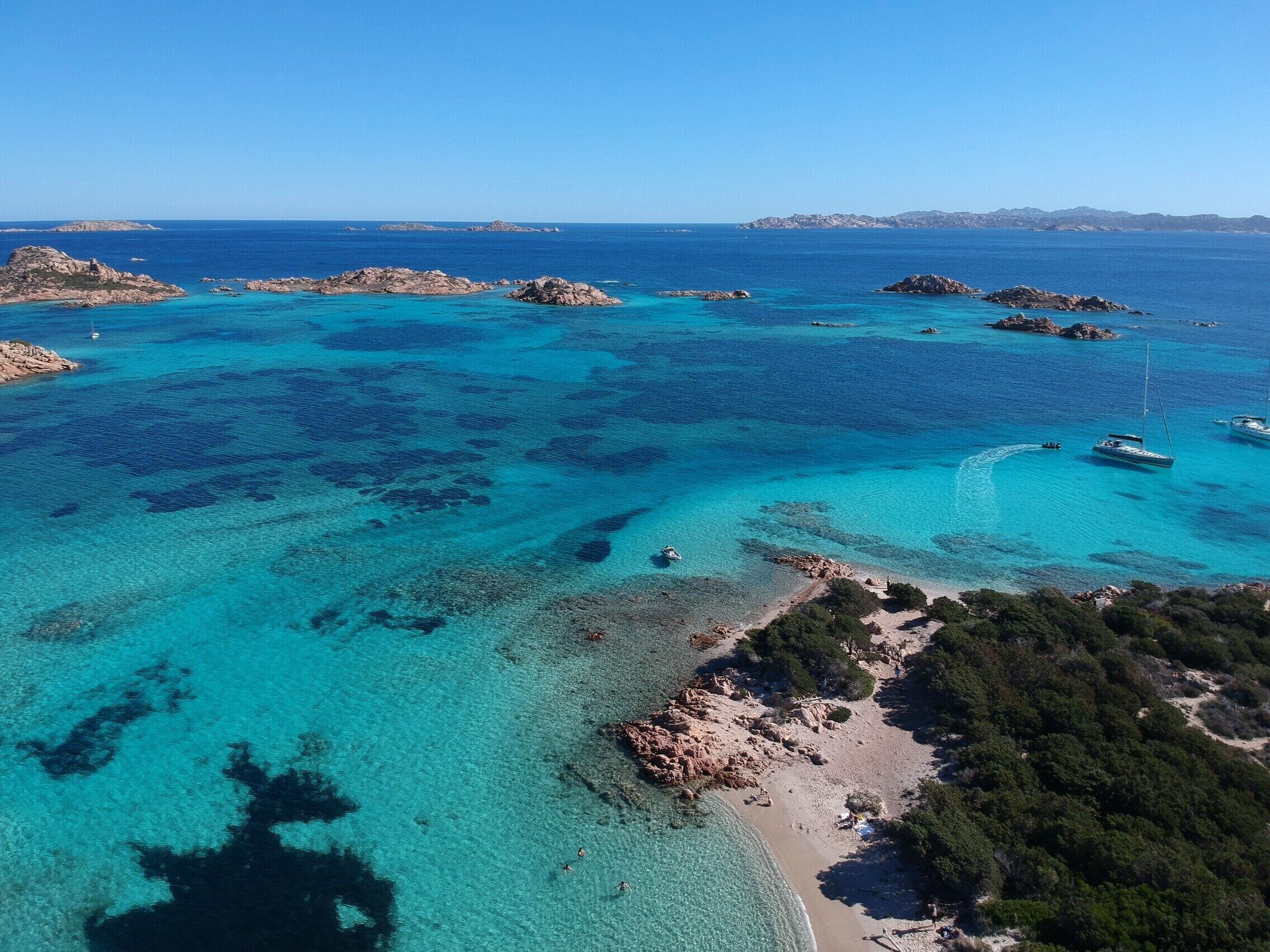 Un paysage côtier caractérisé par des eaux turquoise limpides, des affleurements rocheux et une plage de sable.