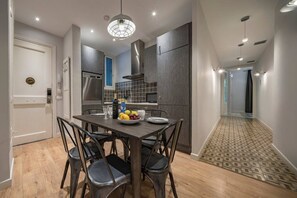 A modern kitchen with a dining table set for four, a fruit bowl, and a bottle of wine.