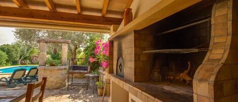 An outdoor patio with a stone barbecue grill, a pool, and lounge chairs.