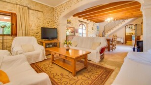 A cozy living room with stone walls, a wooden coffee table, white sofas, and a TV. - Large rustic finca Can Nyany Buger in Mallorca (Buger)