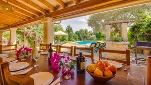 An outdoor dining area with wooden tables, chairs, and a pool in the background. - Large rustic finca Can Nyany Buger in Mallorca (Buger)