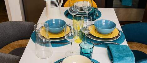 Een eettafel gedekt met blauwe en gele borden, glazen en een karaf.