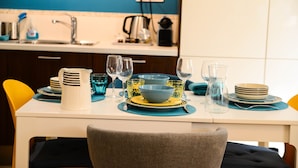 A dining table set with plates, bowls, glasses, and a kettle in a modern kitchen with blue walls and yellow chairs. - Charming town house Avignon intra muros (Avignon)