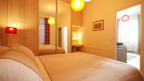 A hotel room with a large bed, a desk, a chair, a mirror, and a window.