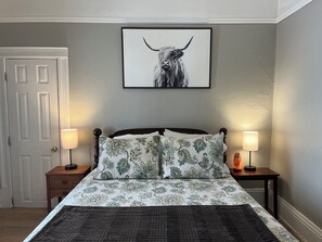 A bedroom with a bed, two nightstands, a door, and a framed picture on the wall.