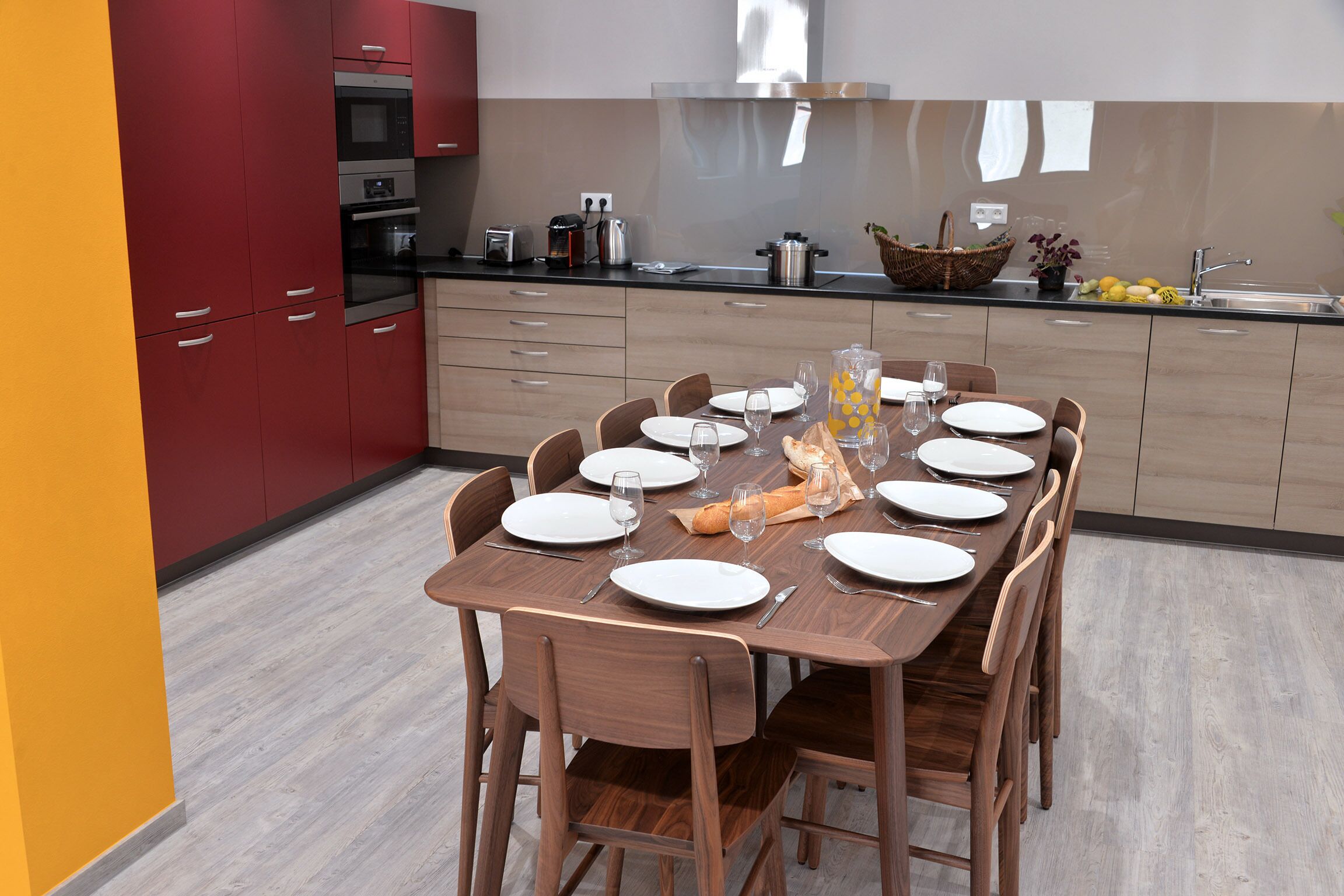 Une cuisine moderne avec des meubles de rangement rouges, une table à manger en bois pour six personnes et un évier en acier inoxydable.