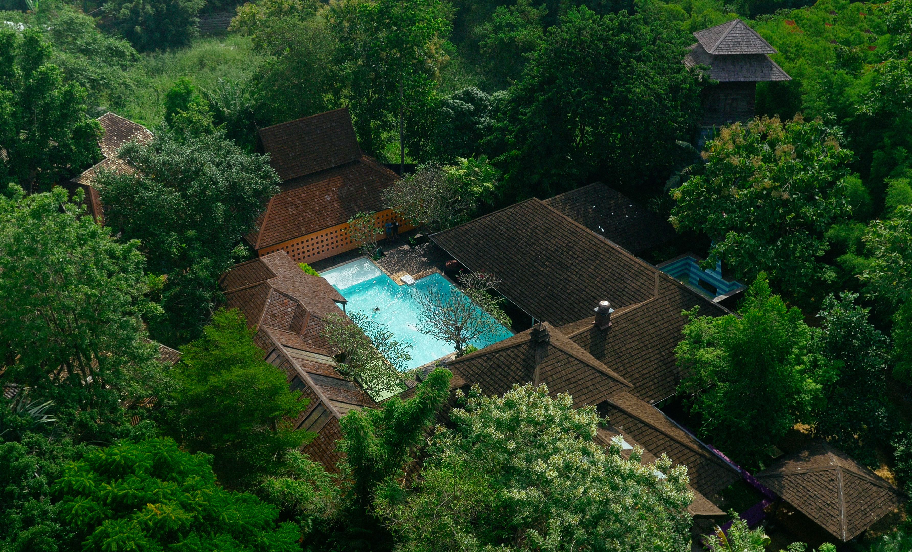 Vista aérea de uma propriedade com piscina, rodeada por vegetação exuberante e vários edifícios com arquitetura tradicional.