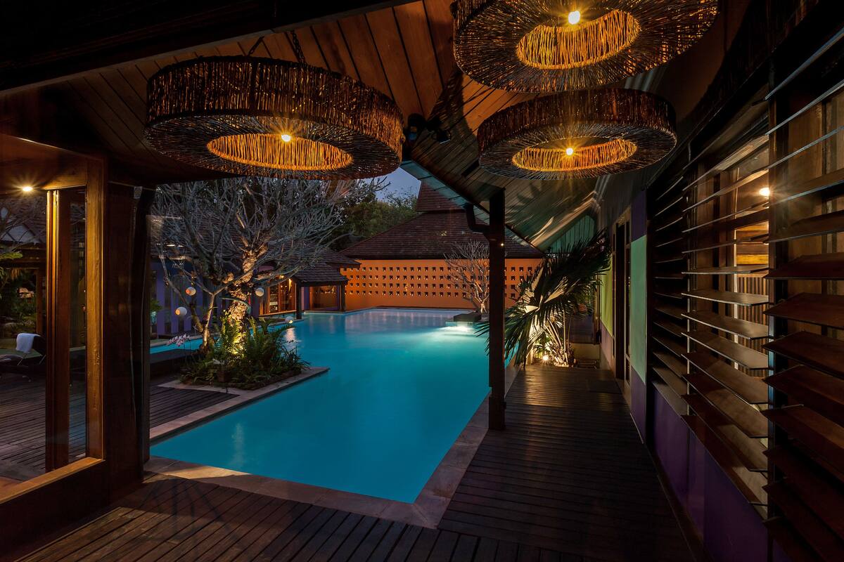 Zona de piscina con cubierta de madera y lámparas colgantes.