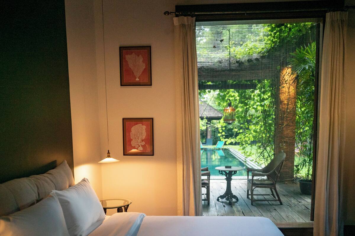 Un dormitorio con cama, mesita de noche, lámpara y vistas a un patio exterior con mesa y sillas.