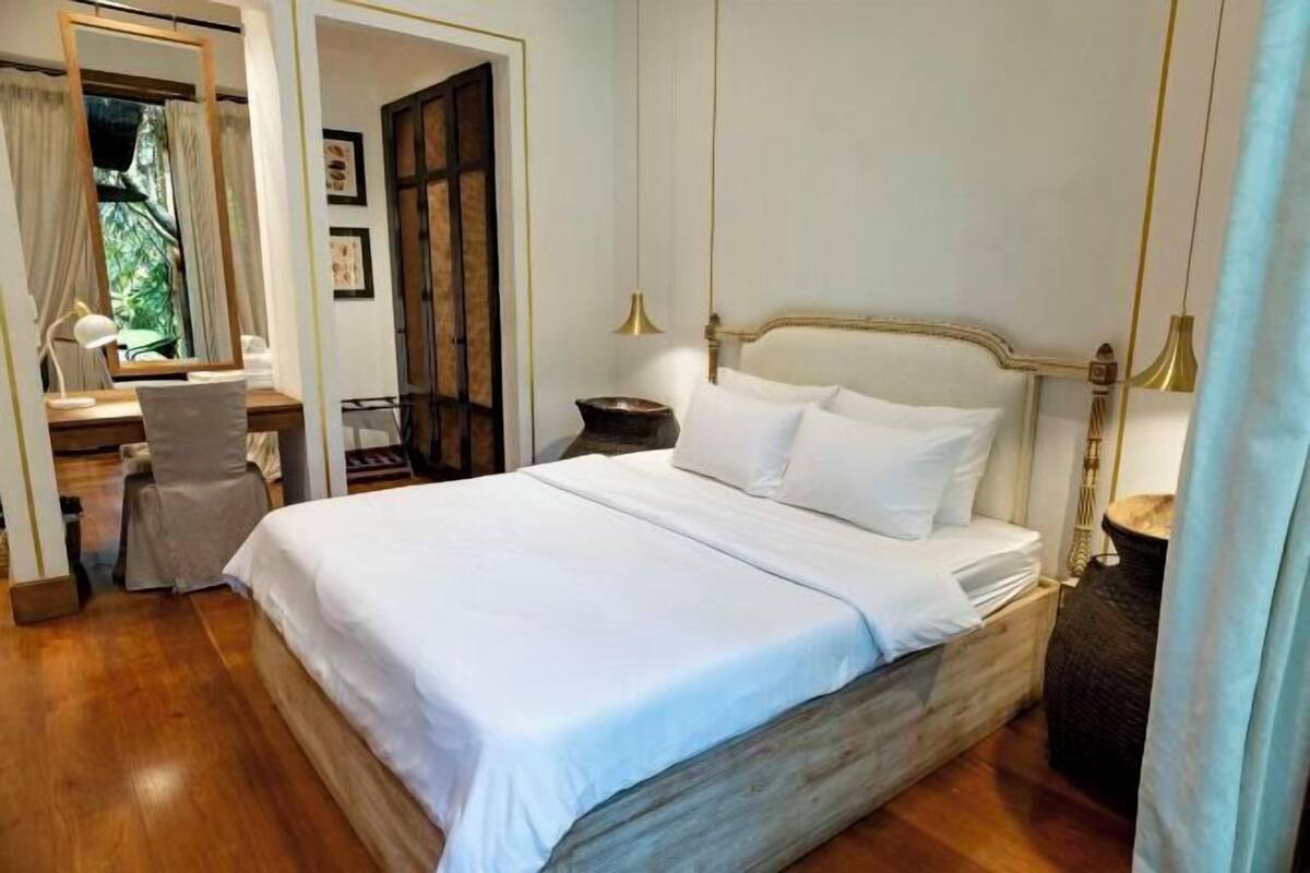 Una cama bien hecha con sábanas blancas, un cabecero de madera y una mesita de noche con una lámpara.