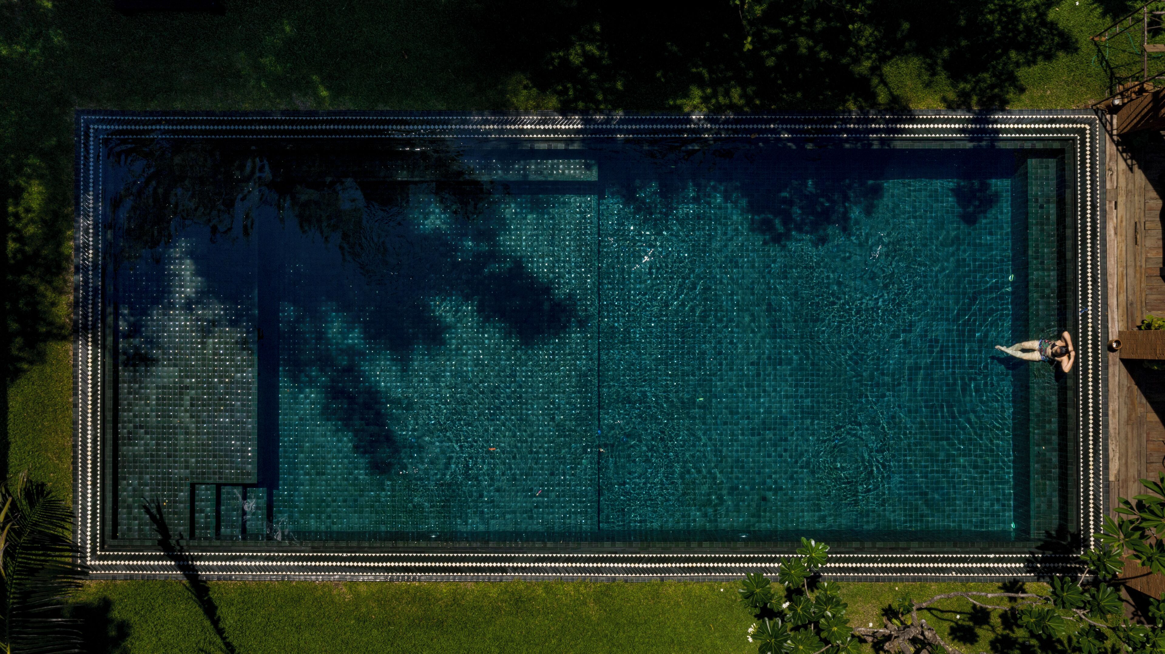 A rectangular swimming pool with a tiled border and a person swimming.