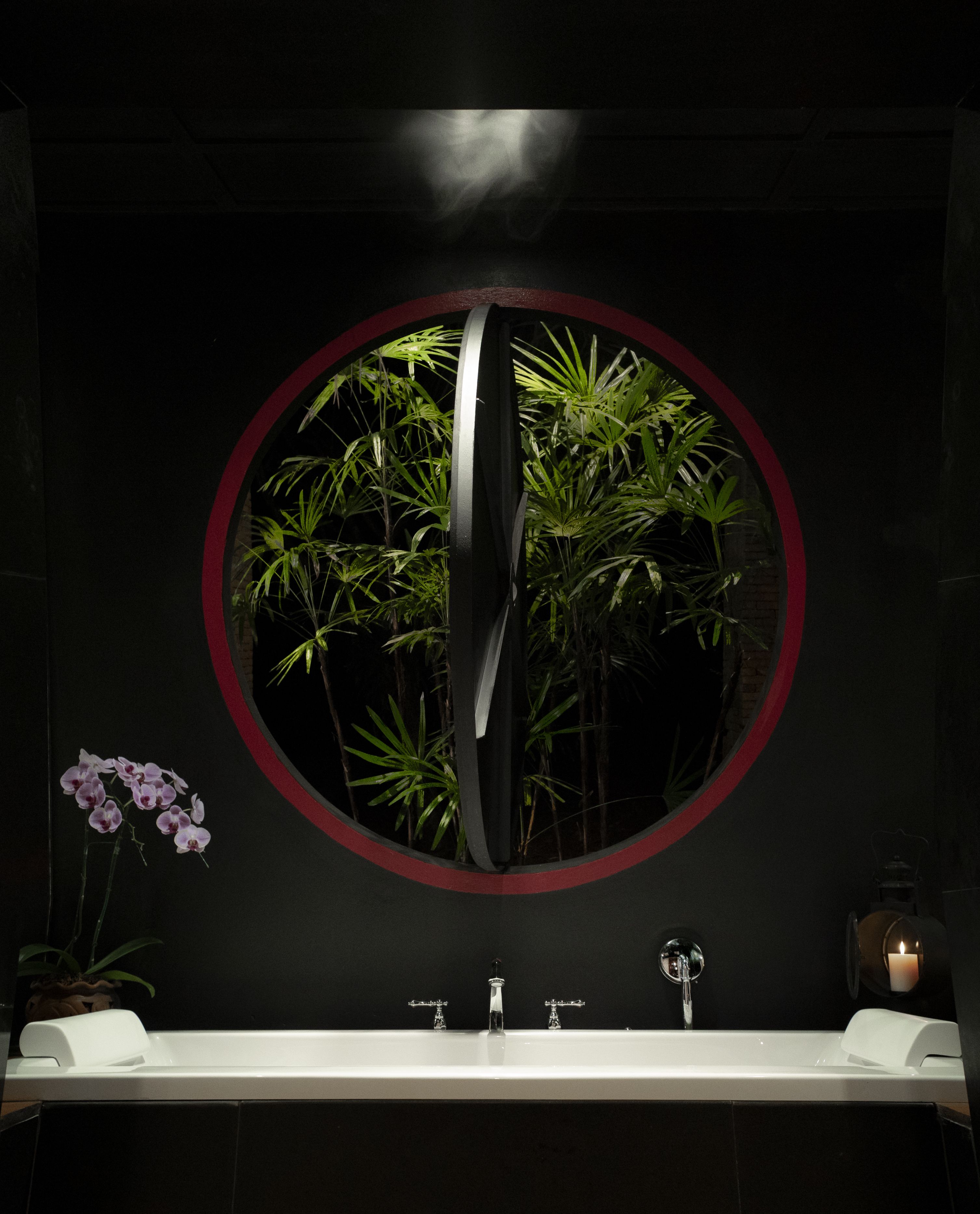 A bathroom with a circular mirror, a sink, and a potted orchid.