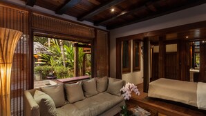 A cozy room with a sofa, a bed, a coffee table, and a window with a view of greenery. - Chandra Residence (Hang Dong)