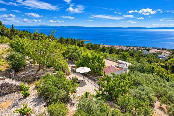 A coastal property with a stone pathway, a white umbrella, and a view of the sea and distant mountains. - Detached house with sea views, on 2. 000qm plot, 2 Schlafzi. (Makarska)
