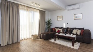 A living room with a brown leather sofa, a wooden coffee table, and a large window with beige curtains. - Detached house with sea views, on 2. 000qm plot, 2 Schlafzi. (Makarska)