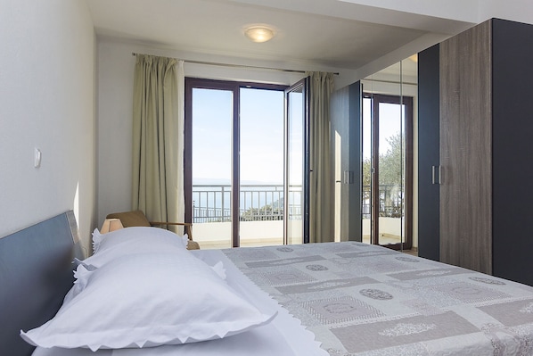 A bedroom with a bed, a nightstand, a lamp, and a view of the outside balcony. - Detached house with sea views, on 2. 000qm plot, 2 Schlafzi. (Makarska)
