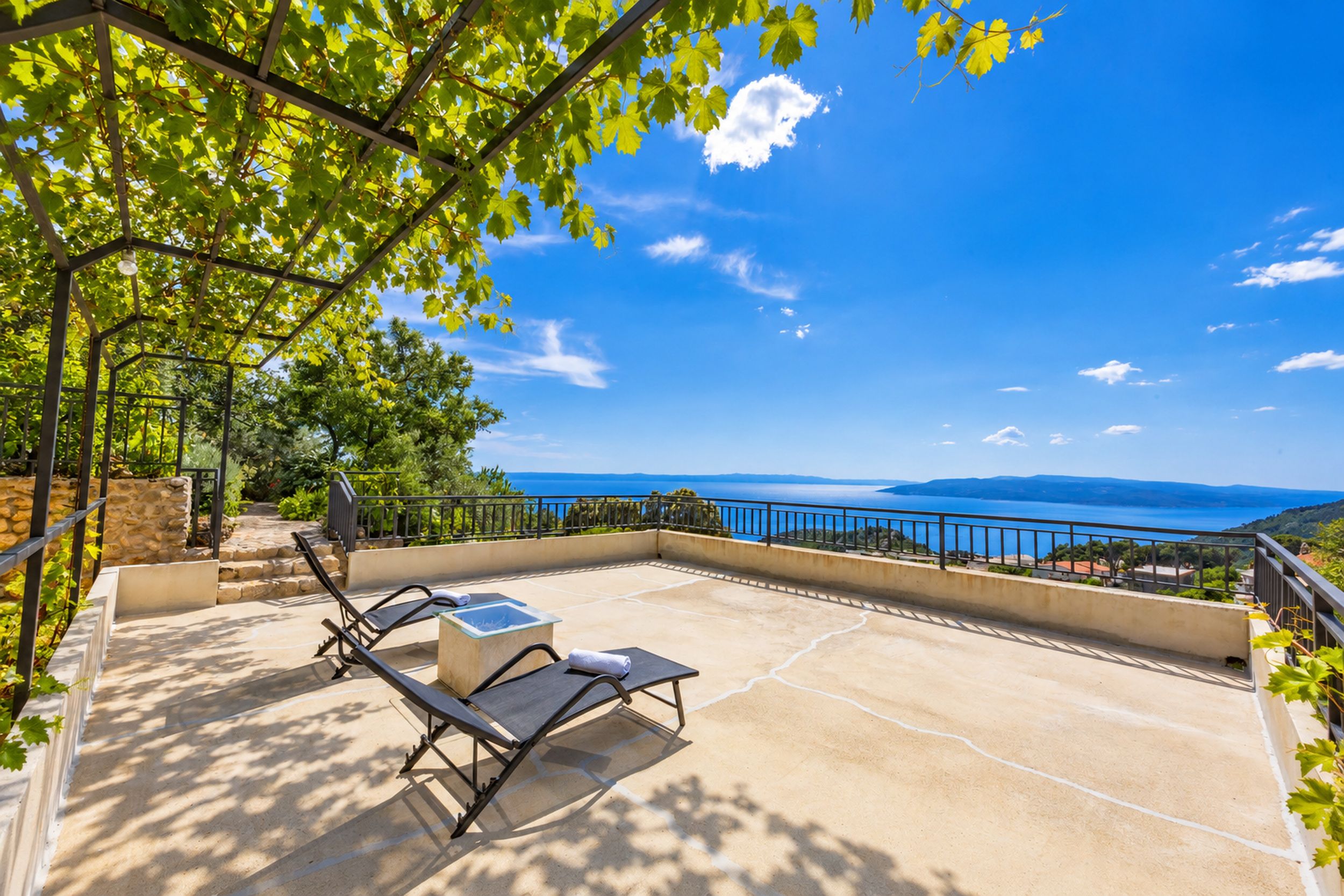 A terrace with two lounge chairs, a small table, and a view of the sea.