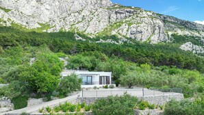 A modern villa with a stone facade, surrounded by lush greenery and a rocky mountain backdrop. - Detached house with sea views, on 2. 000qm plot, 2 Schlafzi. (Makarska)