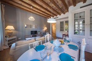 A dining area with a round table set for four, a television in the background, and a wooden ceiling.